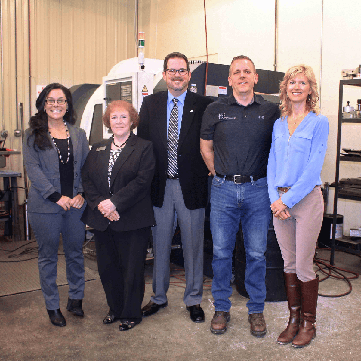 Five people posing together in an industrial facility in front of a CNC machine.