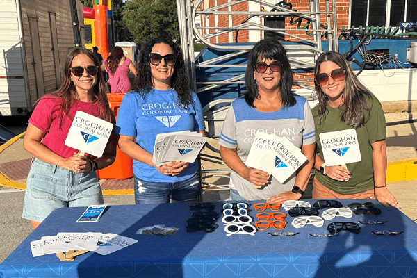 Four Croghan Colonial Bank team members at an outdoor community event table with branded giveaways