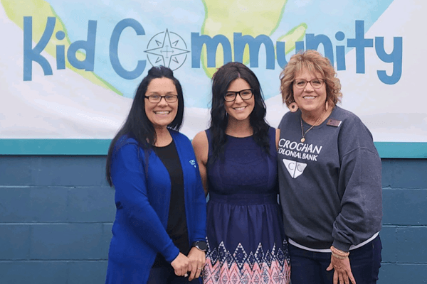Three Croghan Colonial Bank employees smiling in front of a Kid Community mural