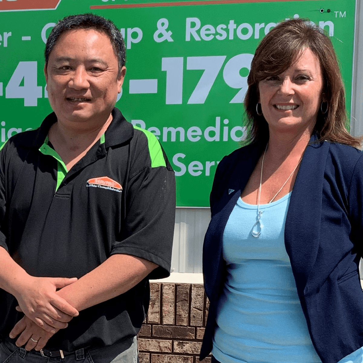 Two people smiling in front of a SERVPRO cleanup and restoration sign, a Croghan Bank business banking client