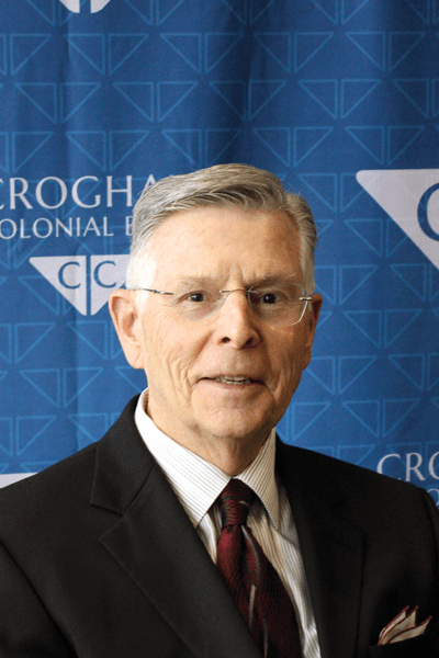 Croghan Bank professional in a dark suit and glasses posed in front of a Croghan Colonial Bank backdrop