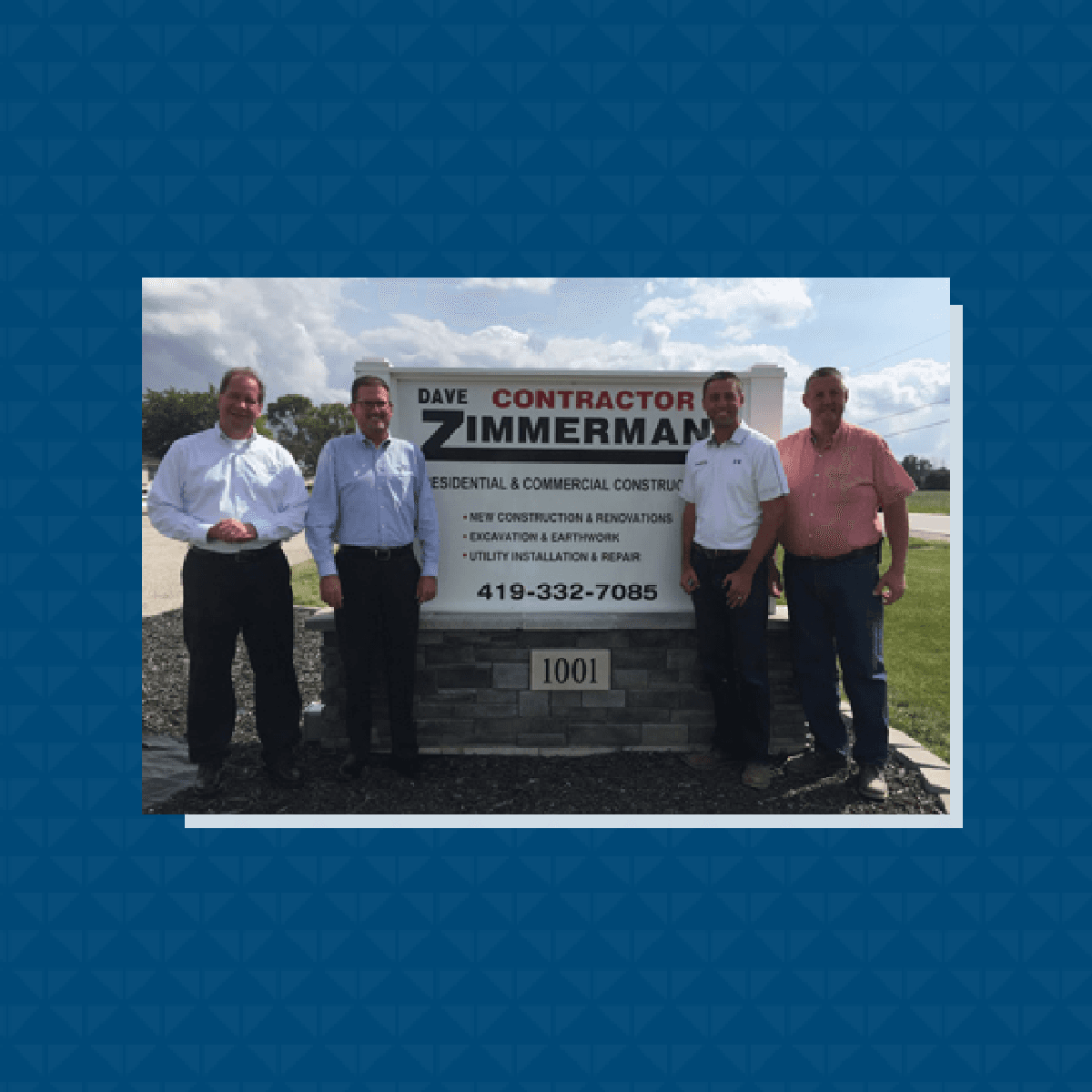 Four people posing outdoors in front of a Dave Zimmermann Contractor business sign.
