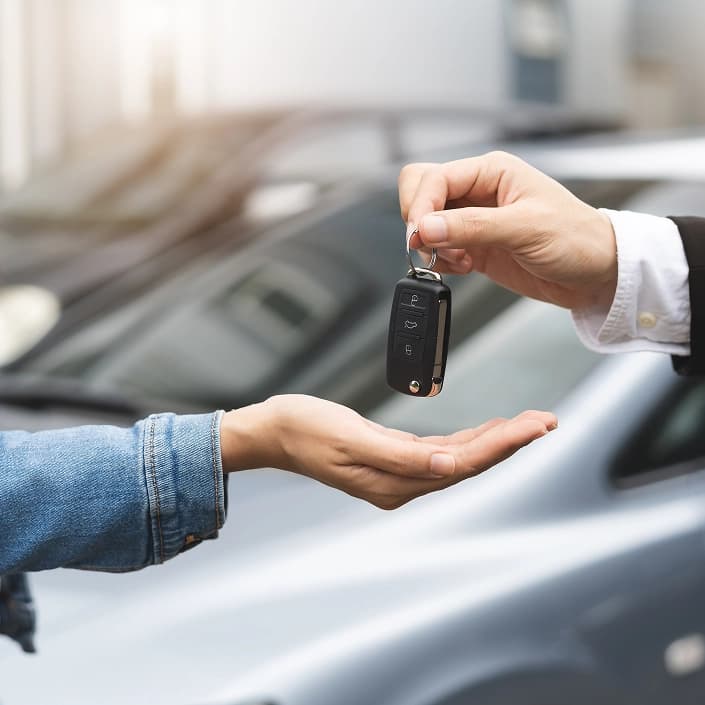 Car dealer handing vehicle keys to a customer outside a dealership, representing an auto loan