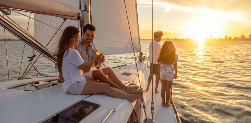 Two couples relaxing on a sailboat at sunset, toasting with drinks on the water
