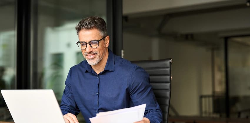 Businessman reviewing financial planning documents while working on a laptop