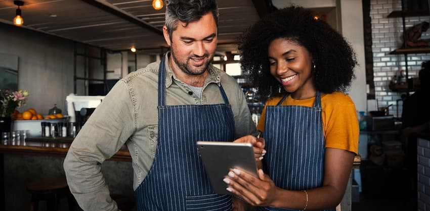 Two café workers in aprons reviewing business banking options on a tablet