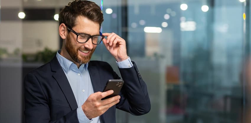 Businessman in glasses smiling while checking his phone for online banking updates