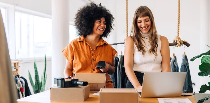 Two small business owners laughing while managing orders on a laptop