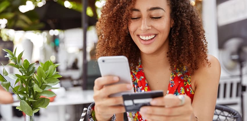 Happy woman holding a credit card and smartphone for online banking