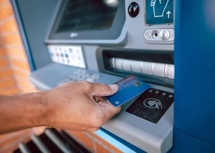 Hand inserting a blue debit card into an ATM machine