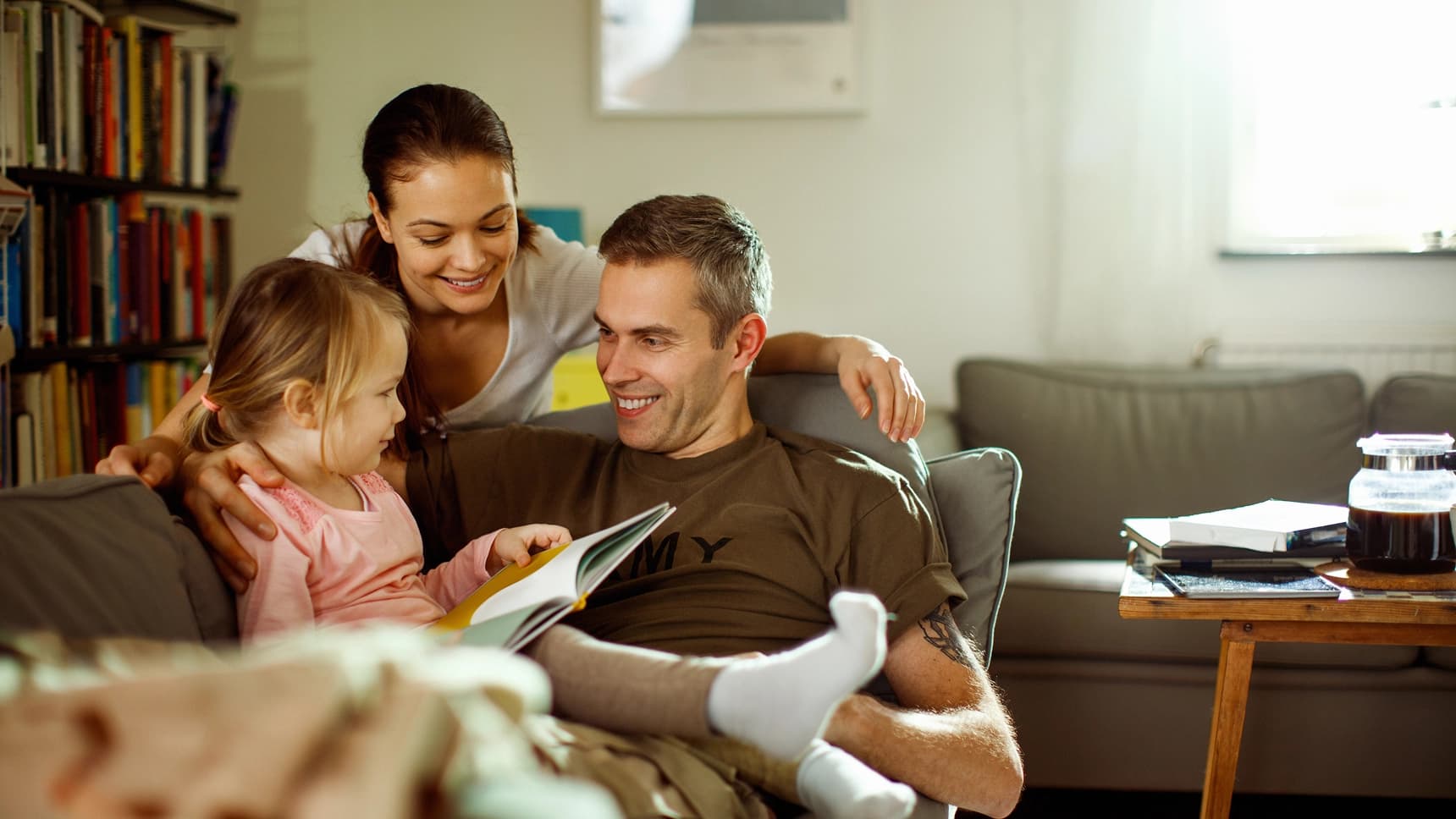 A smiling family reading a book together on a couch in a cozy living room