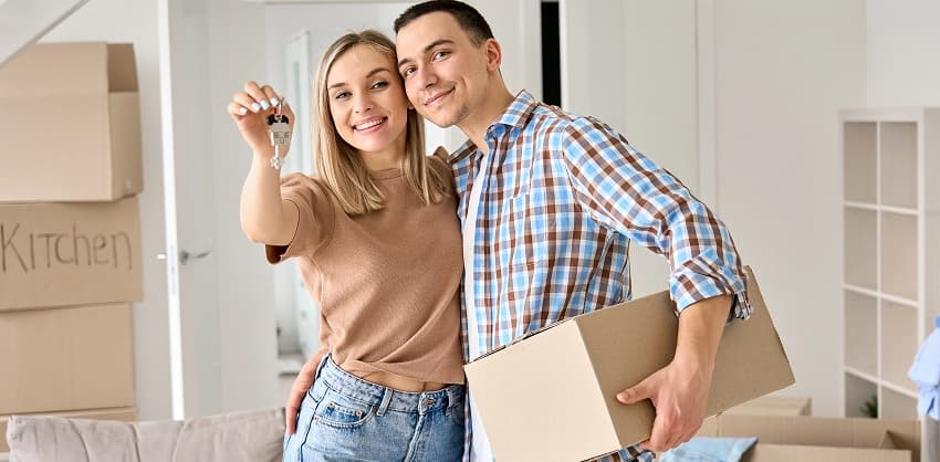 Smiling couple holding house keys and a moving box in their new home