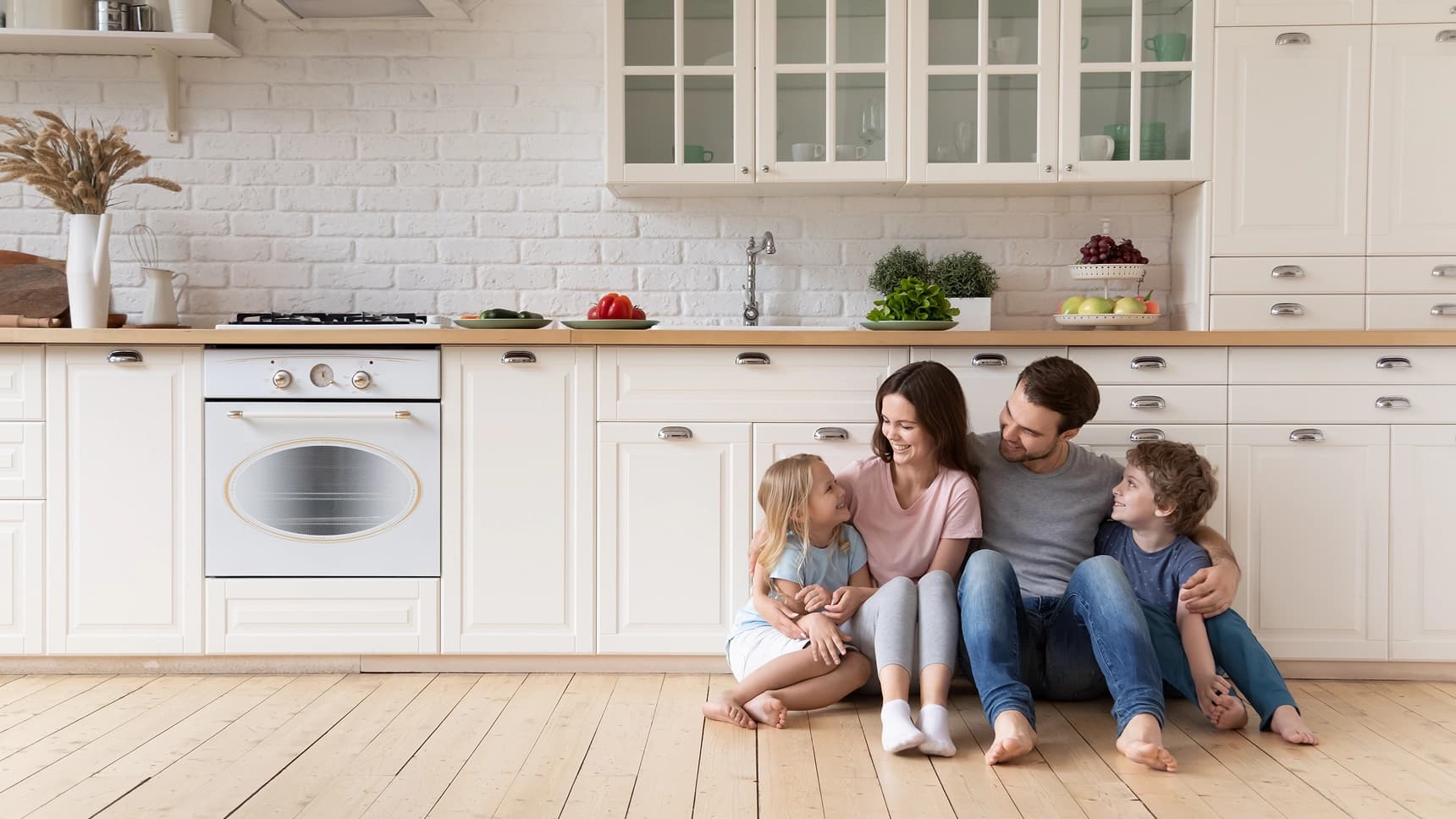 Happy family sitting together on kitchen floor in a bright, modern white kitchen