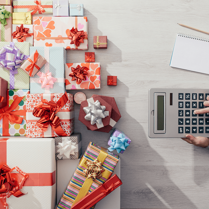Colorful wrapped gifts and a calculator on a wooden surface, representing holiday budget planning and personal loans.