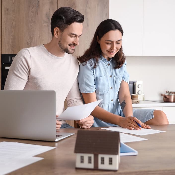 Couple reviewing mortgage loan documents together at home with a laptop and small house model on the table