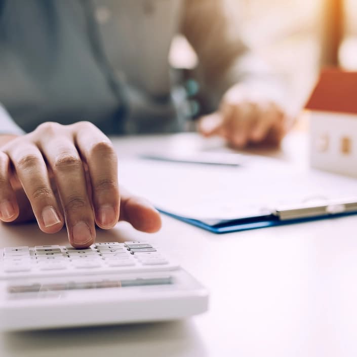 Person using a calculator next to mortgage loan documents and a small house model on a desk