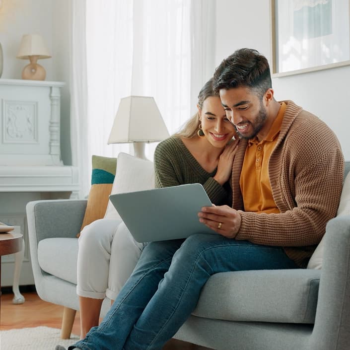 Couple smiling while browsing a laptop together on a couch at home