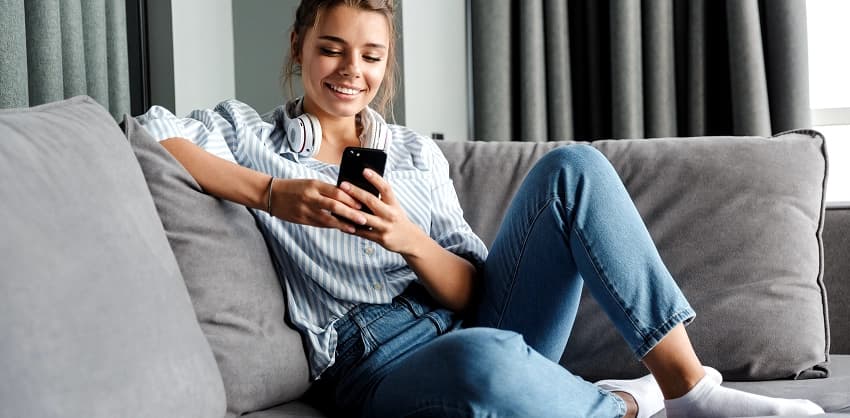 Young woman relaxing on a sofa, smiling while using her smartphone