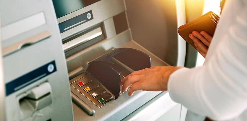 Person using a card at an ATM machine while holding a wallet