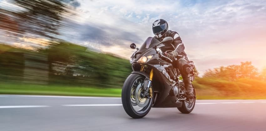 Motorcyclist in full gear riding a sport bike at high speed on an open road