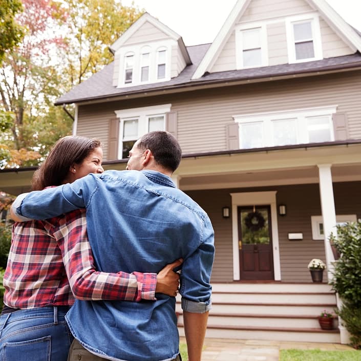 A couple embracing while admiring their new home from the front yard