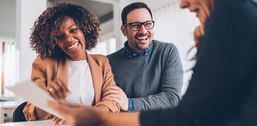 Smiling couple laughing with a financial advisor while reviewing mortgage loan or financial planning documents.