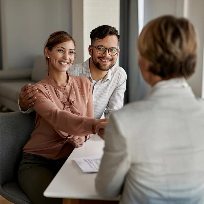 Couple smiling and shaking hands with a mortgage loan advisor at a bank meeting
