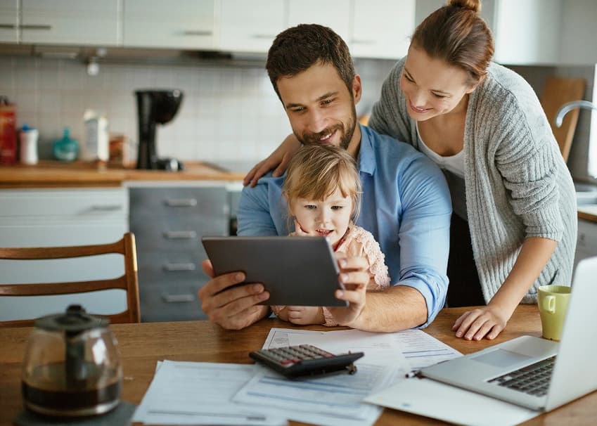 Happy family reviewing finances on a tablet at their kitchen table