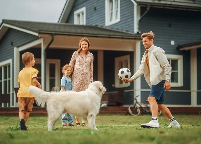 Family playing soccer with their dog in the yard of their blue home