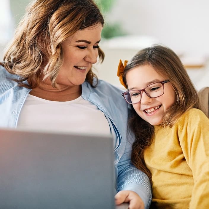 A woman and young girl smiling while using a laptop together at home for online banking