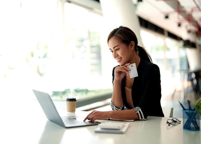 Woman smiling while using a credit card for online banking on her laptop