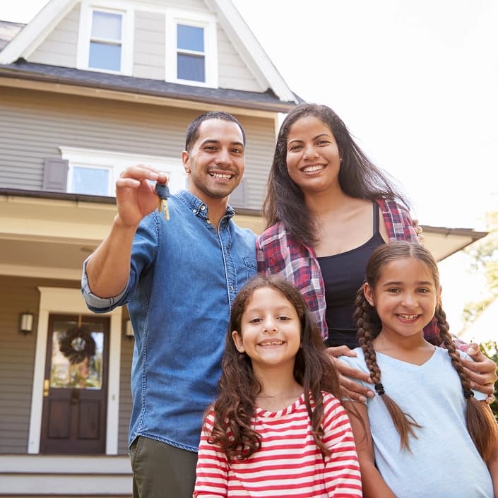 Family smiling in front of their new house, holding keys after closing on a mortgage loan