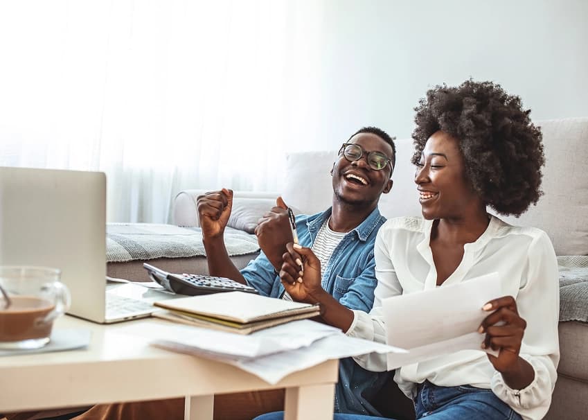 Couple smiling and celebrating good news while reviewing financial documents and a laptop at home