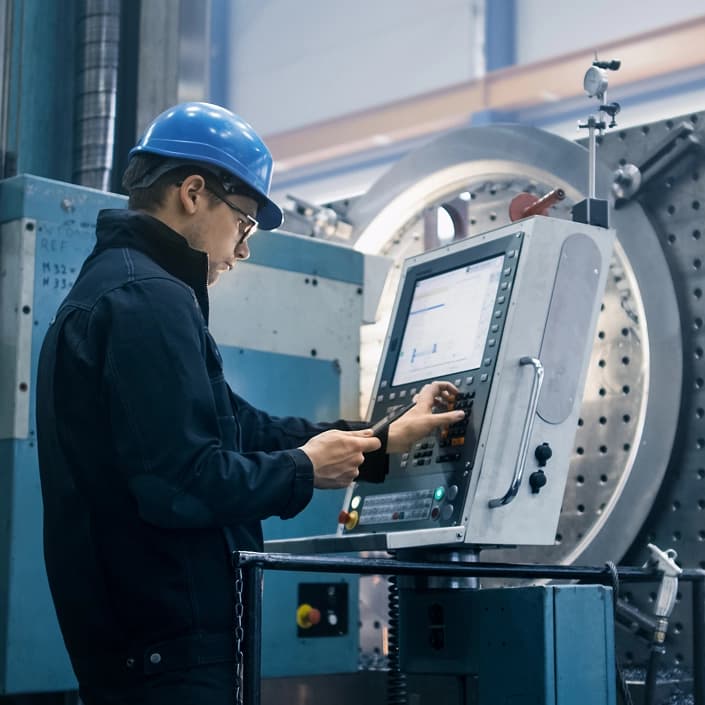Engineer in a blue hard hat operating a CNC machine control panel in a manufacturing facility