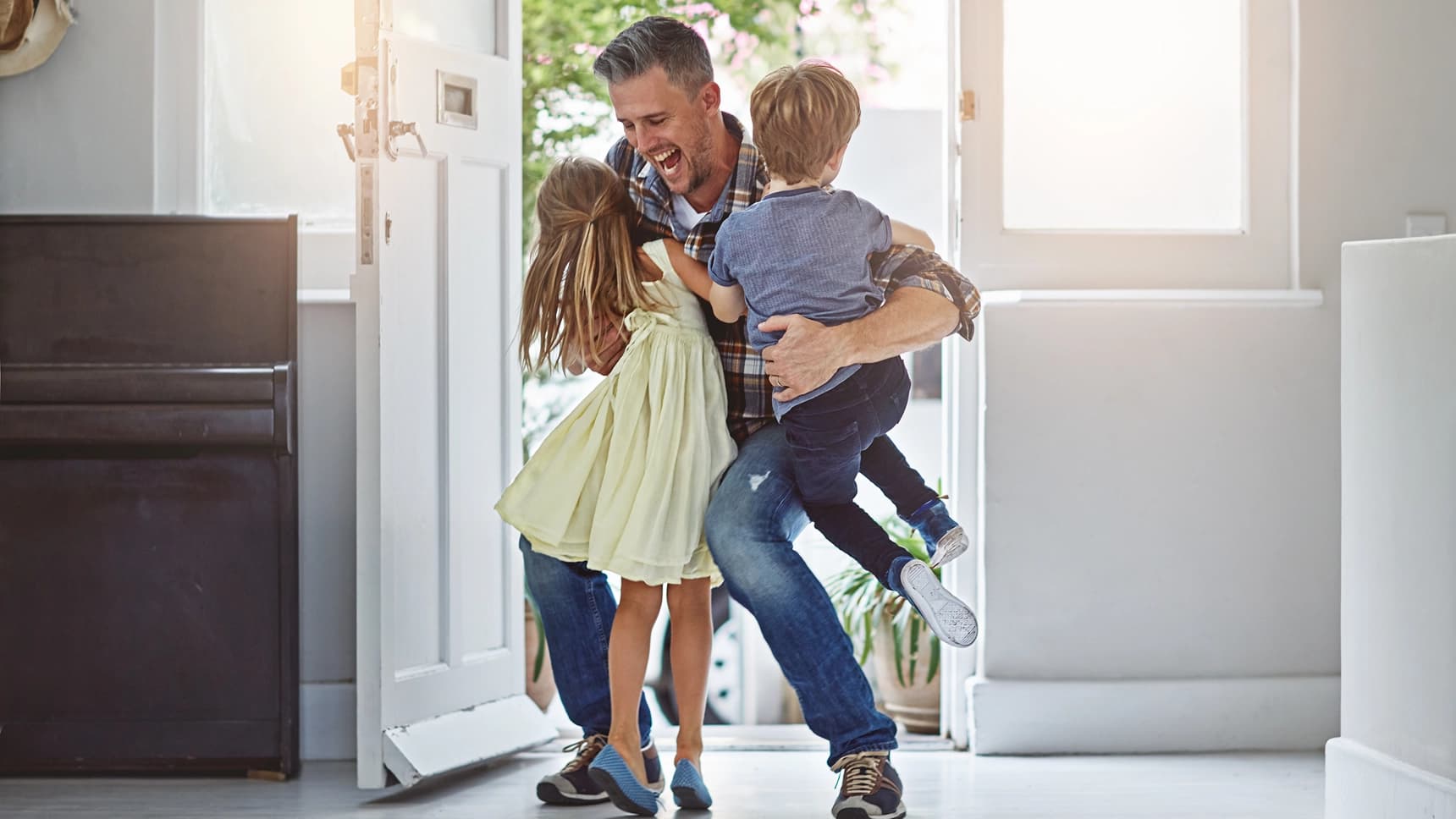 Joyful father being greeted by his children at the front door of their home