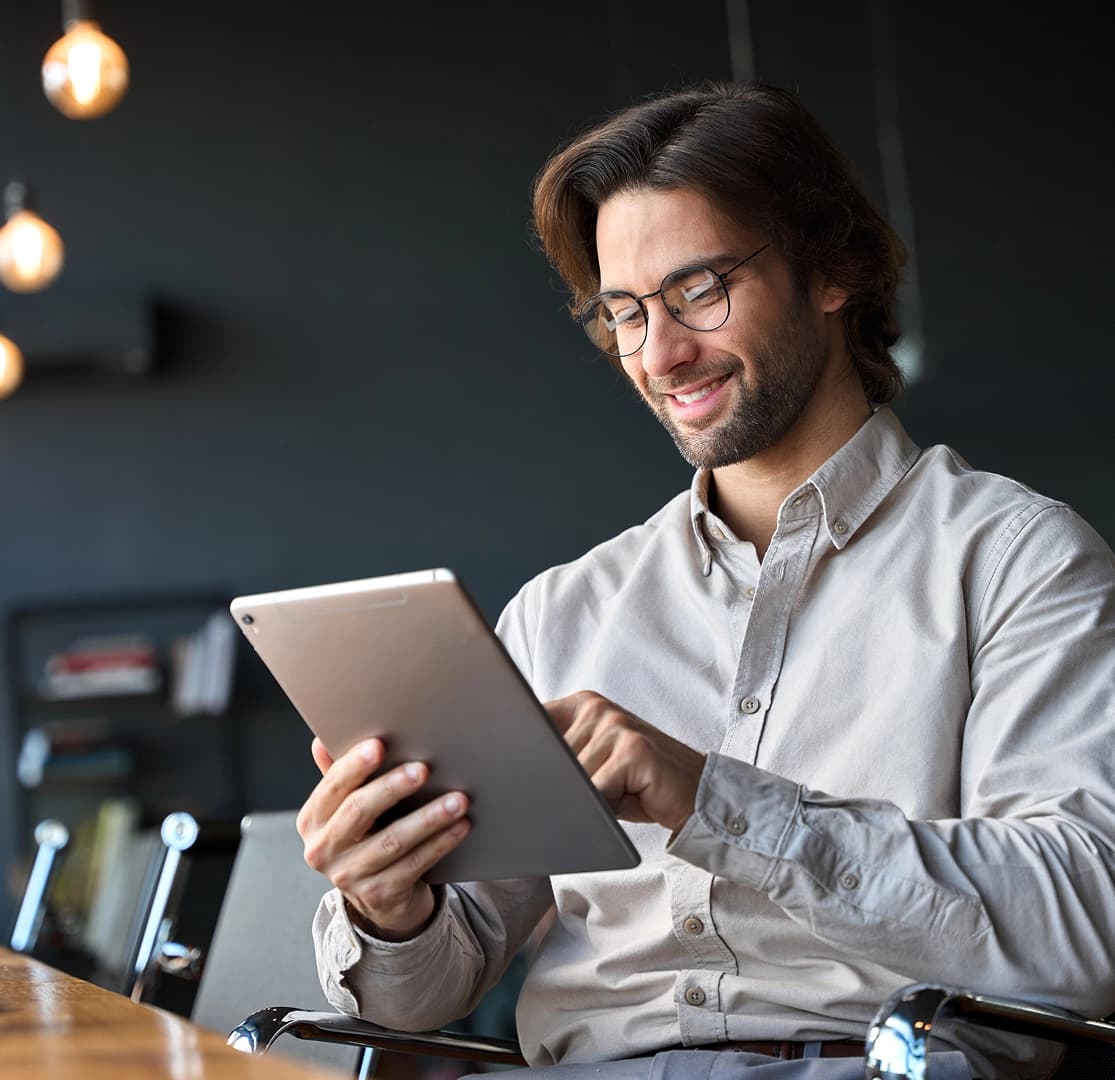 Smiling man with glasses using a tablet for online banking in a modern setting.