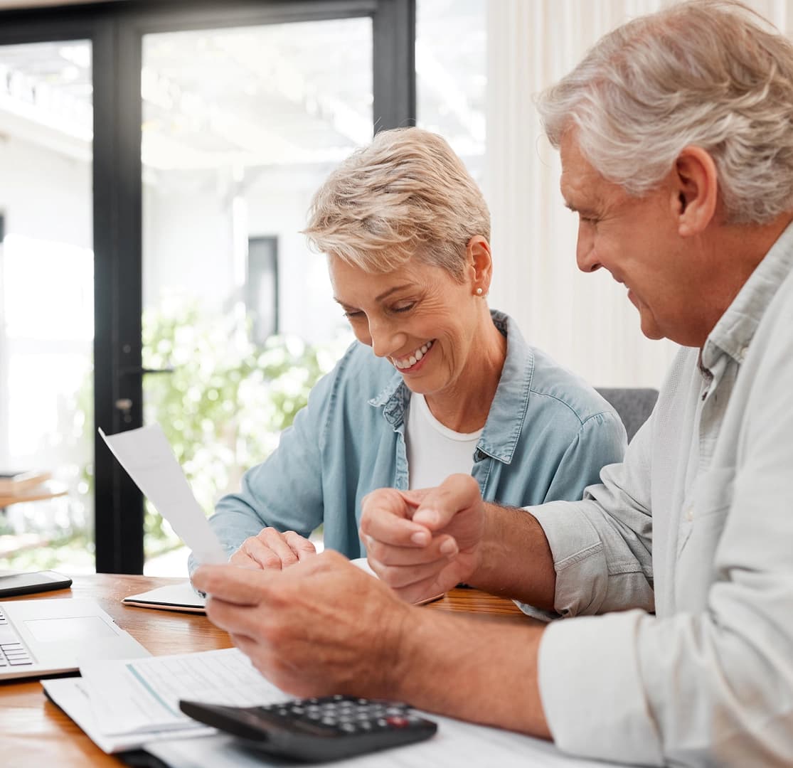 Smiling couple reviewing financial documents and planning together at a home desk with a calculator.