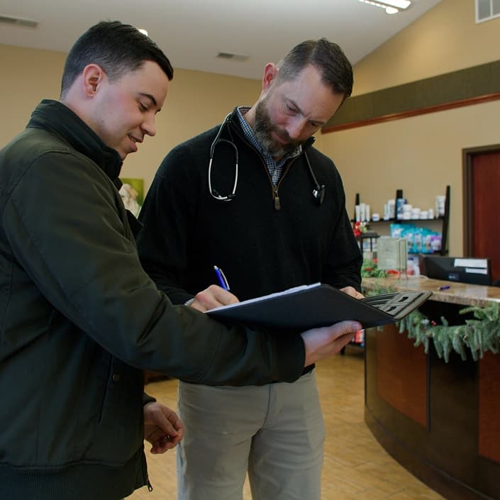 A doctor with a stethoscope reviewing paperwork on a clipboard with a patient in a medical office