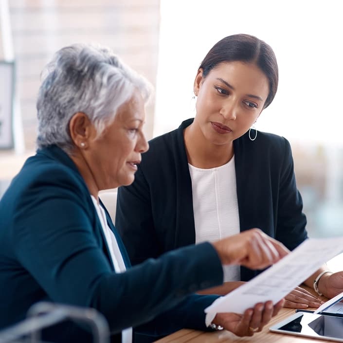 Two professional women reviewing documents together at a desk for wealth management consultation