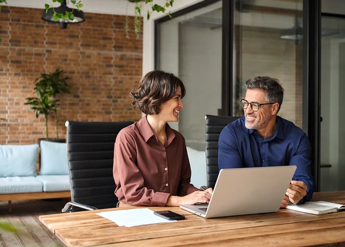 Two colleagues smiling while reviewing financial planning information on a laptop