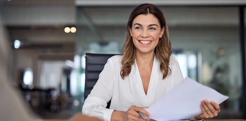 Smiling businesswoman holding documents at her office desk