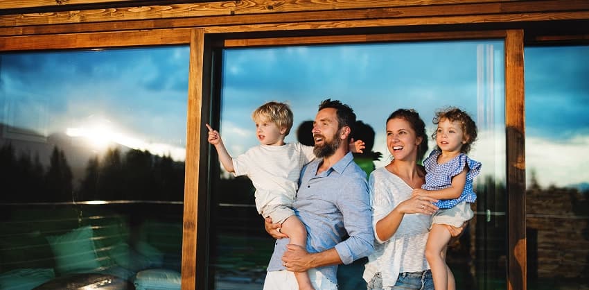 A happy family with two young children looking out a large window at a scenic outdoor view