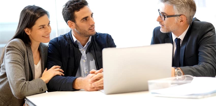 Couple meeting with a financial advisor to discuss mortgage loan options at a desk with a laptop