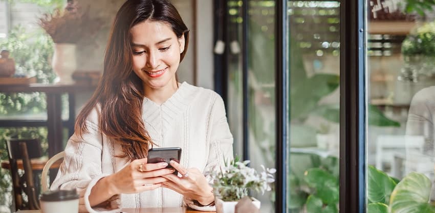 Smiling woman using mobile banking on her smartphone at a café