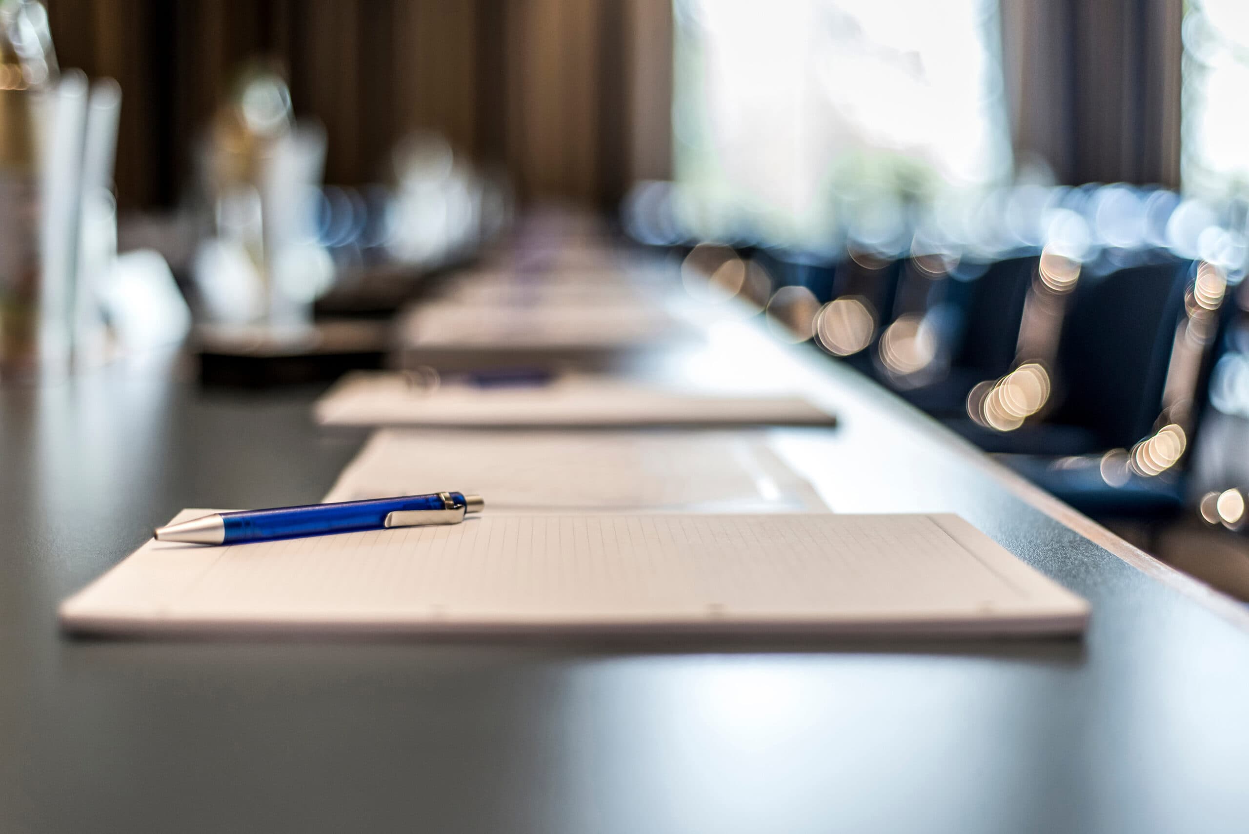 Long conference table with notepads and a blue pen, set up for a business meeting