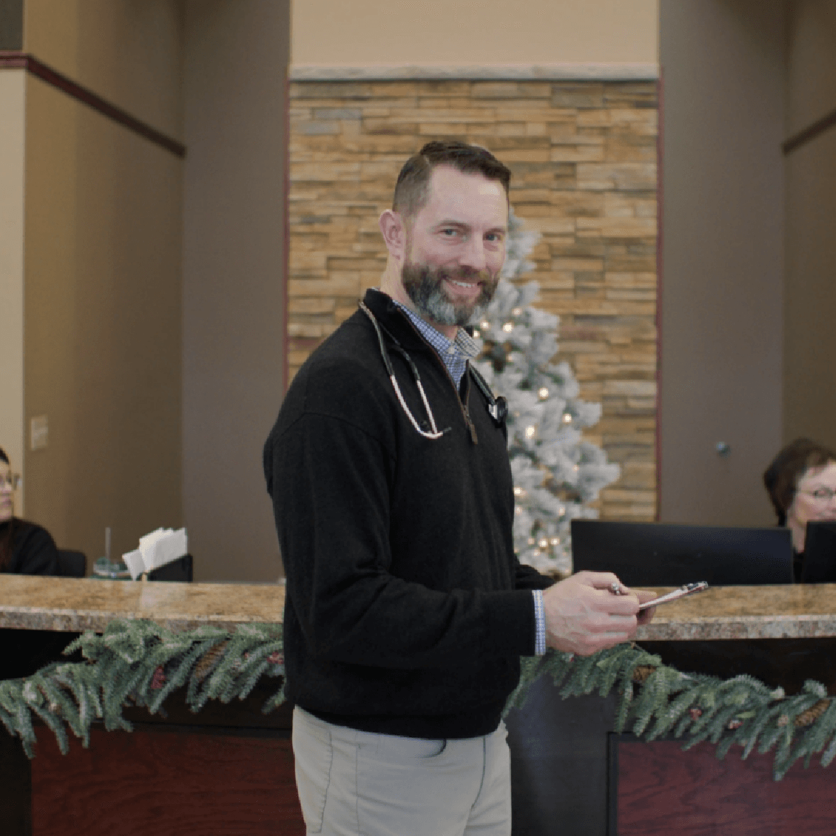 Bearded healthcare professional with stethoscope standing in a decorated medical office lobby
