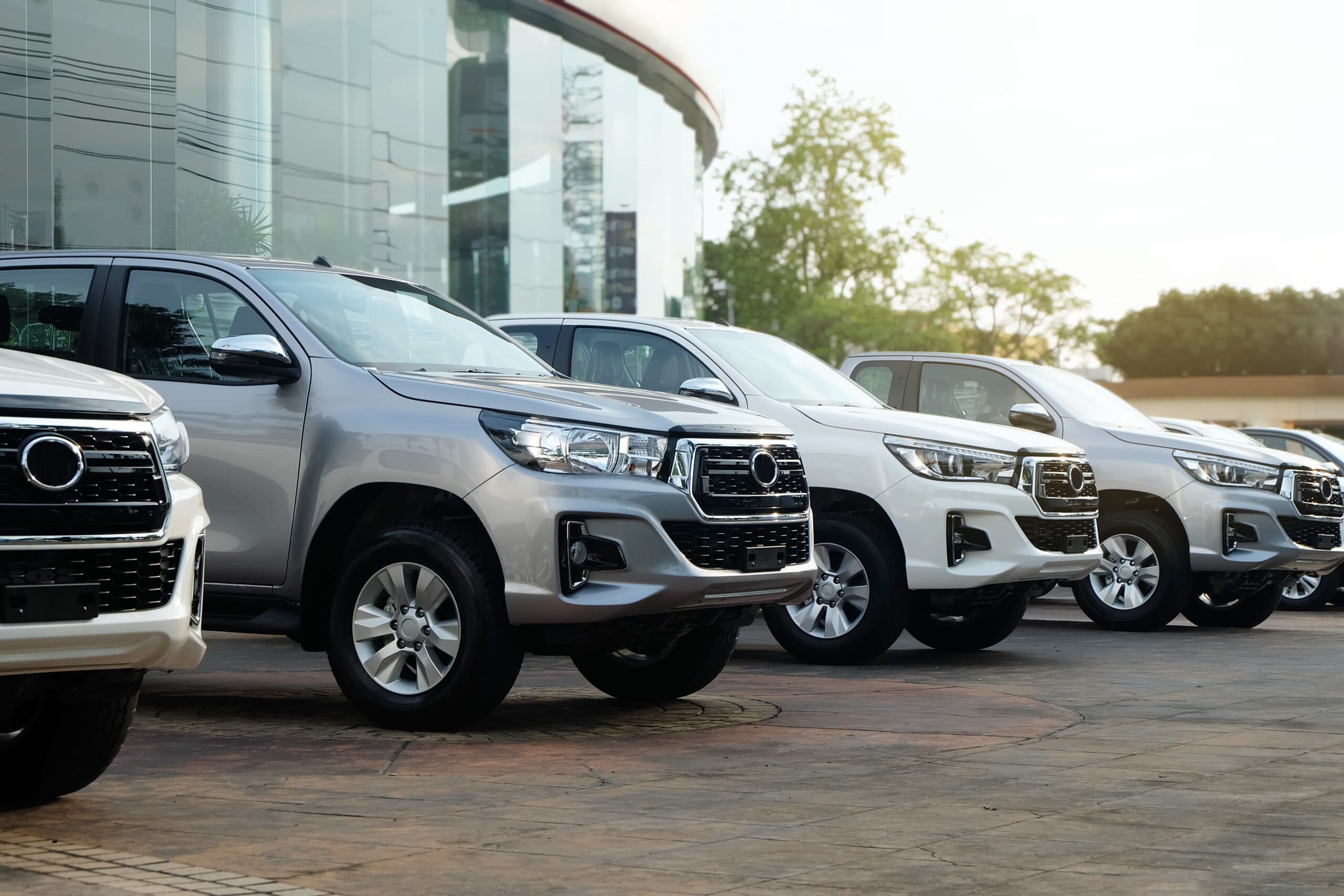 Row of silver and white Toyota Hilux pickup trucks parked outside a dealership showroom