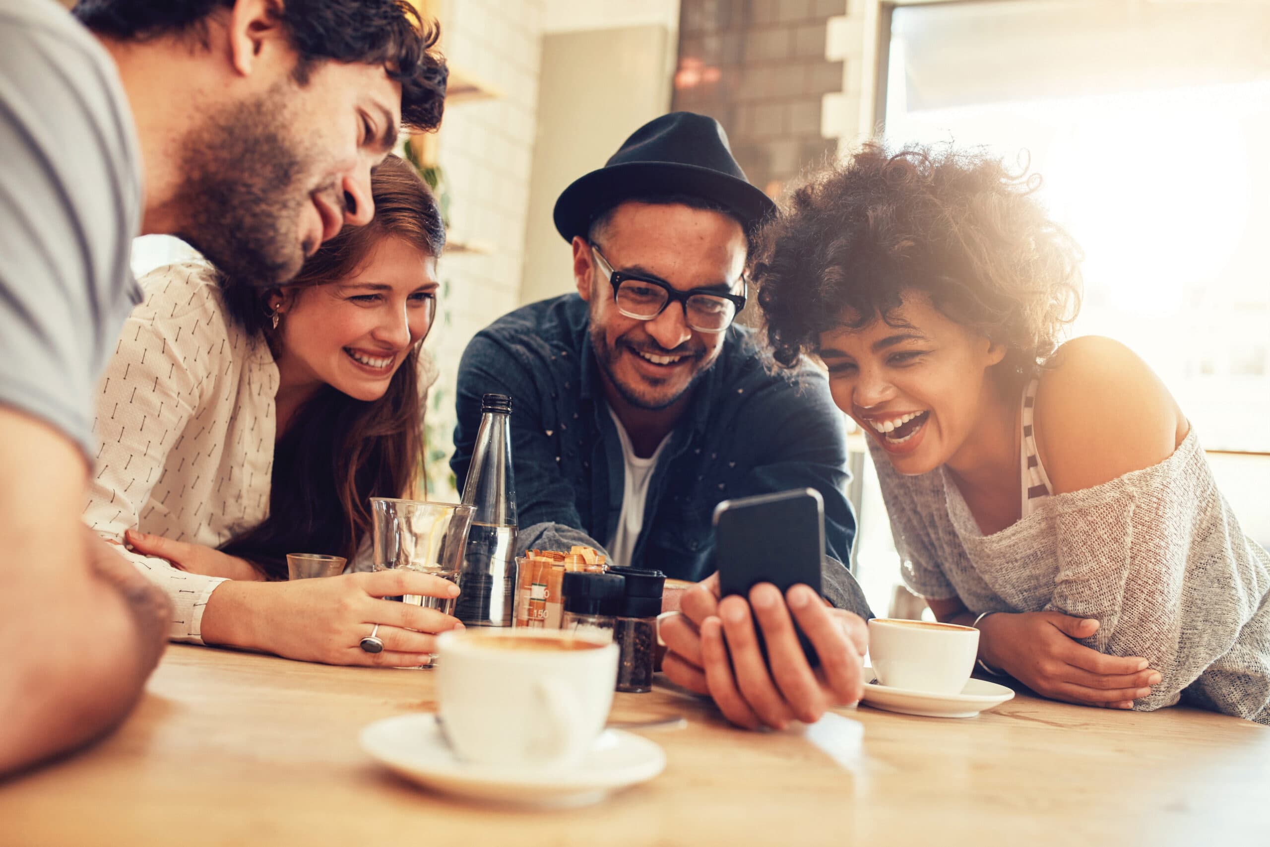 Group of friends smiling and sharing a smartphone at a café table