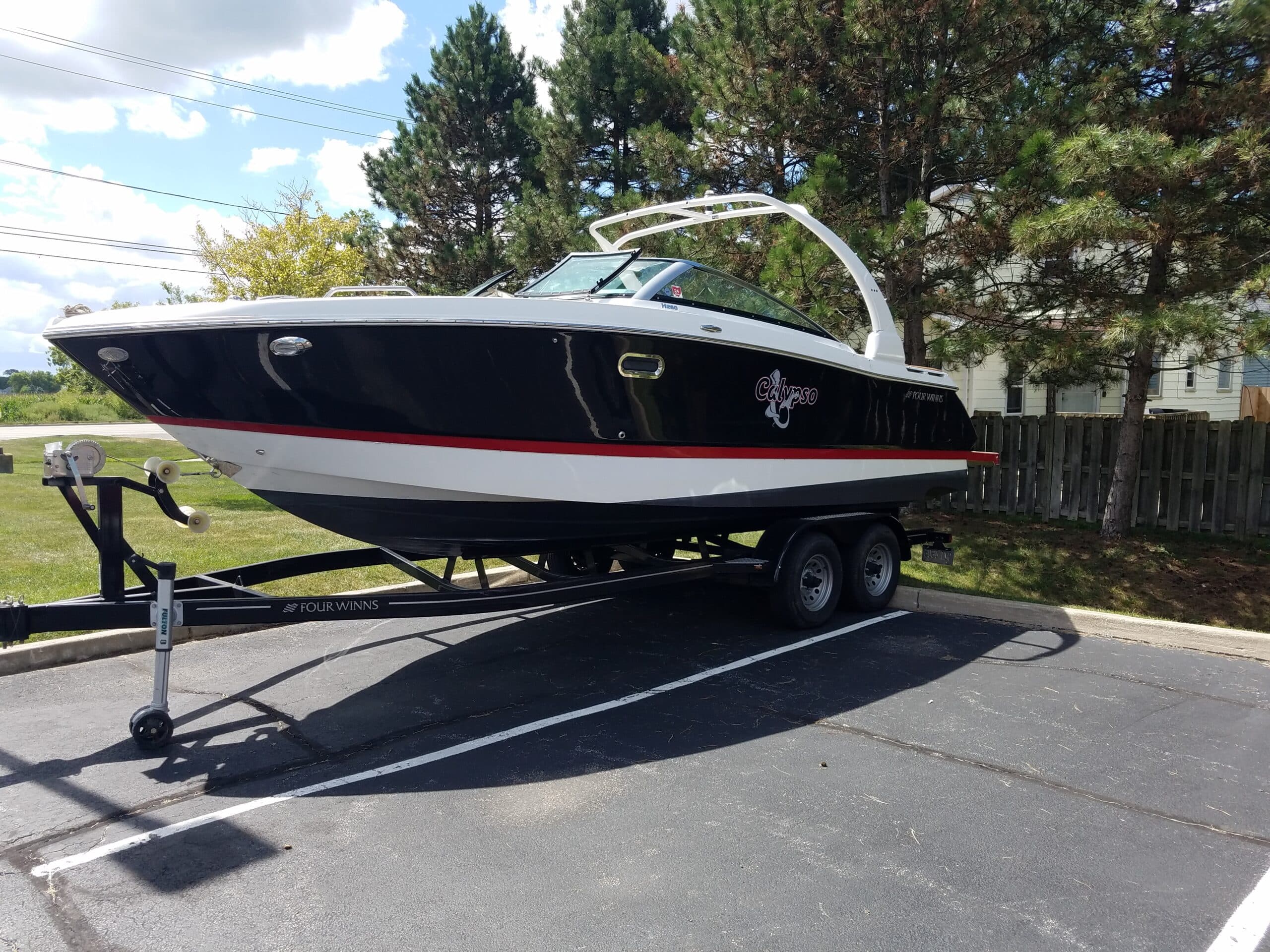 Black and white Four Winns Calypso boat named "Calypso" on a trailer in a parking lot.