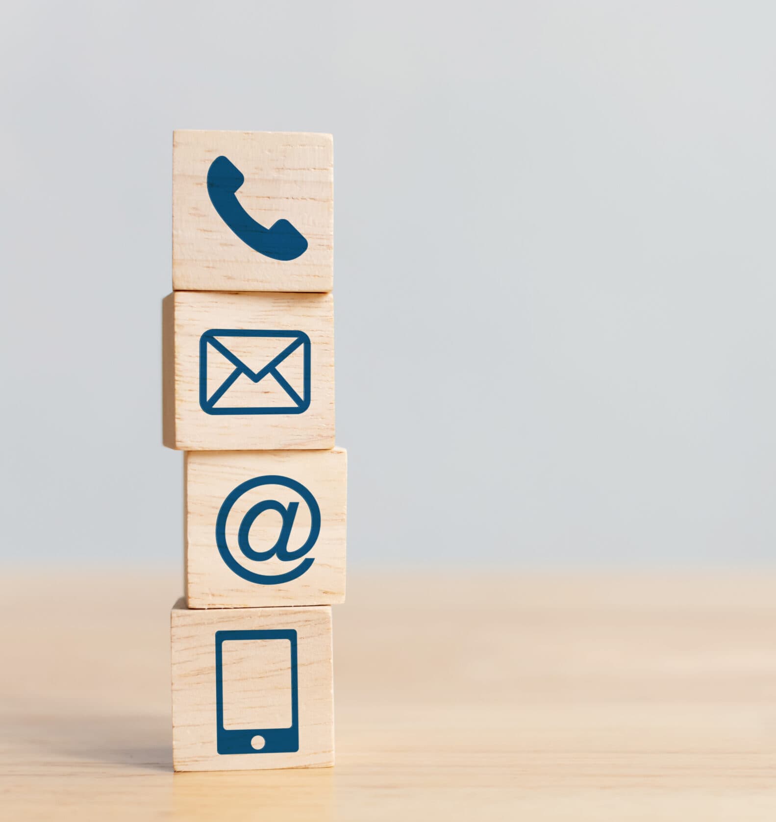 Wooden blocks stacked vertically displaying phone, email, at-sign, and mobile contact icons